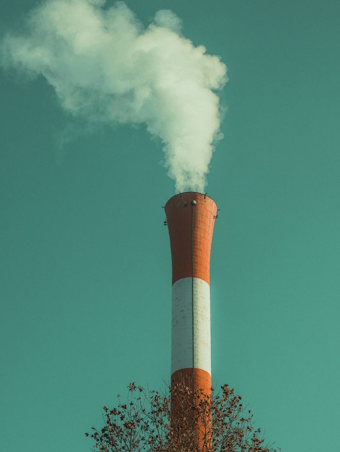 A solitary smokestack emits white smoke into a clear green sky, symbolizing industrial pollution.