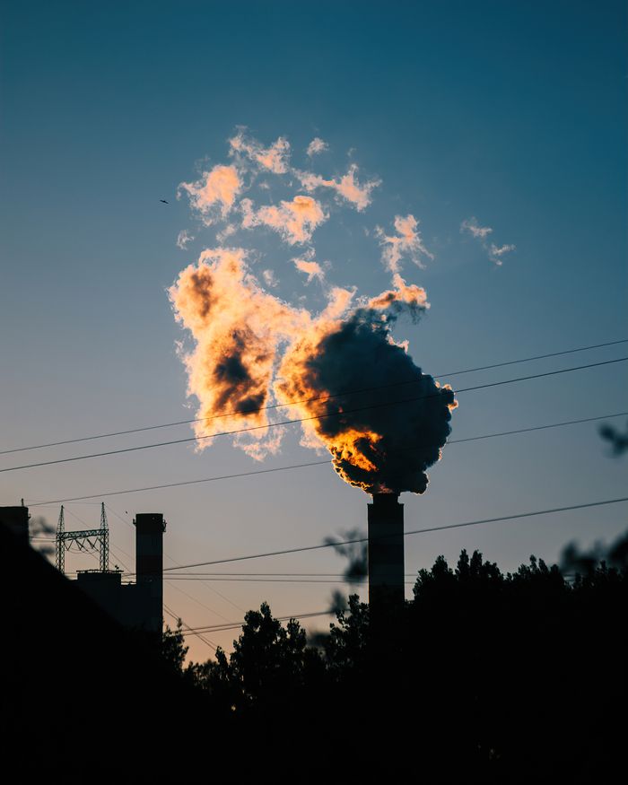 Dramatic industrial smokestacks emit smoke at sunset in Konin, Poland.
